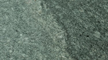 Abstract photography of light reflecting off a polished stone surface. Sage green and charcoal green tones. Sophisticated simplicity, South Asian / Global Professional aesthetic.