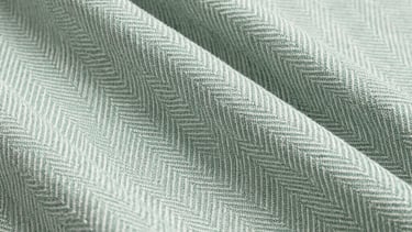 Close-up of a high-quality cotton fabric with a subtle herringbone pattern. Sage green and paper white colors. Professional still life photography.