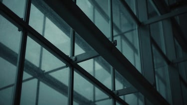 Macro shot of structured glass and architectural steel reflecting cool teal light, low-key dark ambient shadows, sharp angles, 35mm
