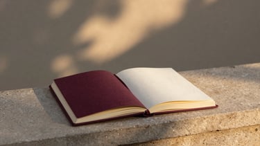 An open linen journal resting on a stone ledge, warm golden-hour light filtering through leaves, quiet textured background, minimalist 35mm photography