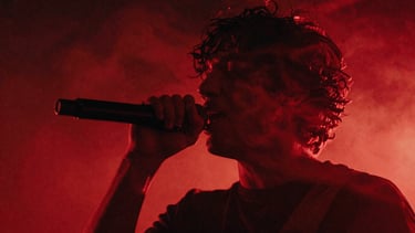 Anamorphic close-up of a musician singing under harsh red neon light, smoke swirling, moody low-light cinematic photography, 35mm grain