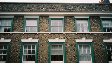 Architectural detail of a classic London brick facade with deep green window frames, soft overcast daylight, desaturated tones, 35mm film