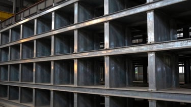 Heavy industrial steel structures neatly aligned inside a manufacturing facility, cool steel tones with high-contrast sharp focus.