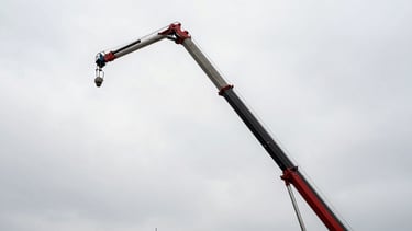 Low-angle heroic shot of a massive concrete pumping boom extending over an industrial construction site, high-contrast overcast sky.