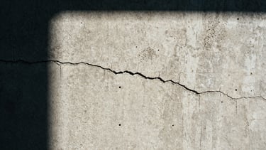 Extreme close-up, high-contrast shot of weathered raw concrete texture, showing cracks and imperfections, under harsh natural light with deep shadows, 35mm film grain.