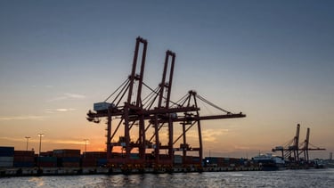 Wide architectural shot of a deep-water shipping port in China at twilight, towering gantry cranes silhouetted against a deep indigo and gold sky, vast container yards extending to the left