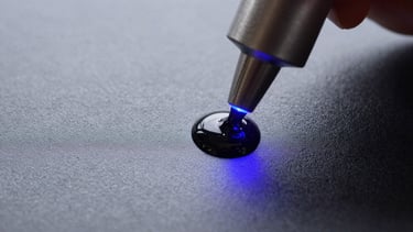 Macro shot of liquid ink droplets curing instantly under UV light on a textured matte vinyl surface.