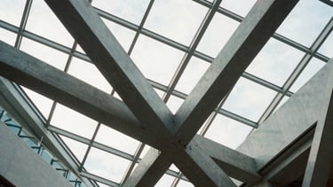 An interior shot of a modern North American atrium with complex geometric glass roofing. Structural steel beams intersect in an elegant, innovative pattern, highlighting the engineering mastery of Mazeej.