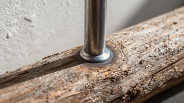 Macro close-up of a clean weld-point on cold-rolled steel, meeting the textured grain of salt-washed driftwood, casting sharp graphic shadows under side daylight.
