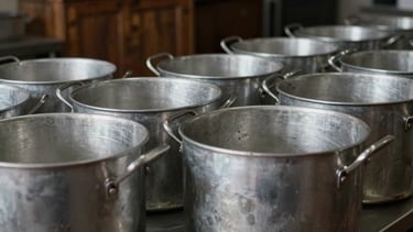Large industrial aluminum stock pots lined up in a clean, professional restaurant kitchen.