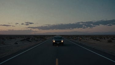 Cinematic 35mm film still, extreme wide shot of a lone car on an endless desert highway under a bruised twilight sky, dramatic low-key lighting.