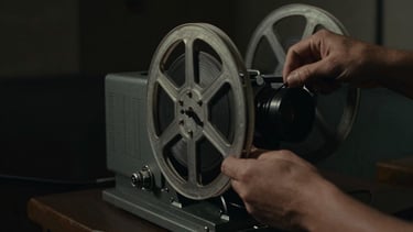 Cinematic film still, dramatic low-key lighting, a close-up of hands threading 35mm celluloid onto a vintage projector in a dark booth.