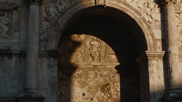 Cinematic film still, high-contrast shadows on a textured stone archway in Rome, warm golden hour light, rich shadows.
