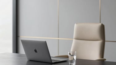 A premium North American executive workspace with a minimalist design. A sleek black desk holds a silver laptop and a glass of water. A comfortable beige leather chair is in the background. The wall is soft gray with a subtle gold accent frame. Natural light spills through clean windows.