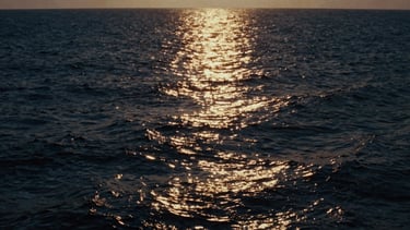 Cinematic film still of a dark ocean horizon with a single glowing golden light rising from the deep water, high contrast, dramatic side-lighting