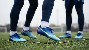 Close-up of athletic gear on turf, soccer cleats stepping on an agility ladder, high-contrast overcast daylight, professional training environment.