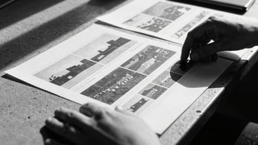 Extreme close-up of hands arranging stark black-and-white editorial layouts on a concrete table, harsh direct sunlight casting deep dramatic shadows, 35mm film grain.