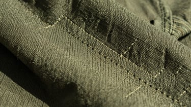 Extreme macro shot of durable pine green canvas fabric, showing detailed custom stitching and rugged texture under natural high-contrast sunlight.