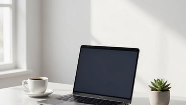 Professional North American / US interior photography of a minimalist workspace. A sleek laptop sits on a light gray desk beside a cup of coffee and a small succulent. The background is a clean white wall with soft morning light from a side window. Sophisticated atmosphere using a palette of white, gray, and deep charcoal.
