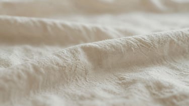 Extreme close-up of a soft organic cotton baby blanket texture in warm cream and muted sage tones, soft diffused natural light, minimalist abstract photography