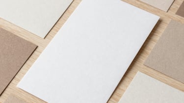 Professional flat lay photography of printed paper samples and digital invitation templates in soft earthy tones and off-white, arranged on a light wood surface.