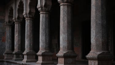 Low-key dramatic side-lighting on the stone pillars of a historic Indian institutional building, high contrast, deep shadows, 50mm