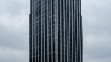 High-angle architectural shot of a financial district skyscraper reaching into cool overcast clouds, sharp clean lines, slate gray and deep navy tones, massive scale.