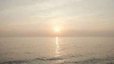 Wide panoramic golden hour shot over Southeast Asian coastline, soft warm sunlight reflecting on calm water, low horizon, serene atmosphere, 35mm film style.
