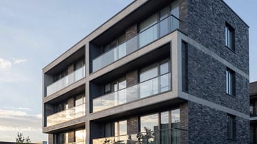 A high-end architectural photograph of a modern residential development project in Newcastle. The building features clean lines, large glass windows, and premium brickwork under a soft Northern European morning light. Professional and trustworthy atmosphere with a palette of deep blues and pale greys.