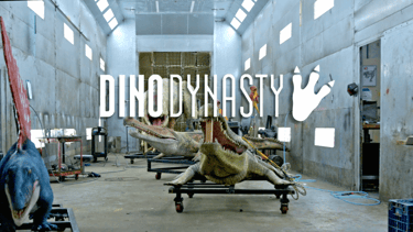 Animatronic dinosaurs including Spinosaurus and Sarcosuchus in a workshop with DinoDynasty logo.