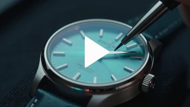 High-end commercial video frame of a luxury watch being polished, dark studio lighting, soft teal reflections on glass, play icon overlay