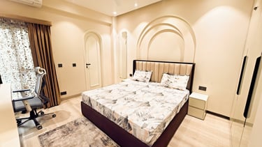 Modern bedroom with an upholstered queen bed, arched wall decor, and an office chair.