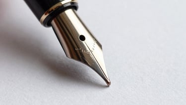A macro shot of a fountain pen nib touching off-white textured paper, symbolizing the precision and uncommon thought in our brand strategies.