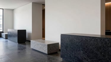 A clean, modern photography shot of a high-end minimalist office lobby in Chicago, North American / US. The scene features polished dark navy stone surfaces and off-white walls with sleek slate gray furniture. Soft, natural morning light creates a professional and sophisticated atmosphere with clear lines and deep focus.
