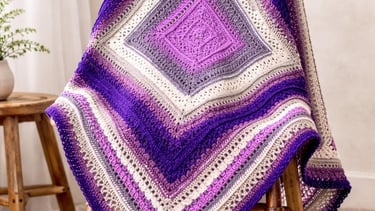 Handmade crochet blanket in purple and cream ombre square pattern draped over a wooden chair.