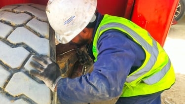 A construction worker in a hard hat and safety vest inspects a heavy machinery tire.