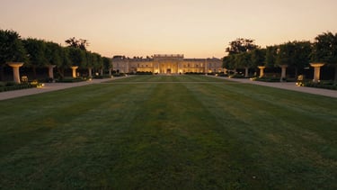 Wide panoramic view of Divine Farms estate grounds at golden hour, manicured lawns stretching into the distance, soft warm twilight, elegant architectural lighting illuminating pathways, low horizon, cinematic.