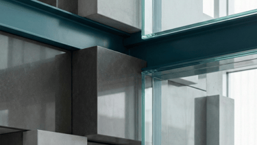 Modern architectural detail featuring geometric concrete blocks and glass panels with teal steel beams.