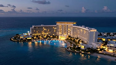 Extreme wide-angle environmental drone shot of a luxury Cancún resort at twilight, deep blue ocean, golden lights reflecting on pools, cinematic composition.