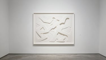 A large framed white papercut sculpture hanging on an empty white gallery wall, soft side shadows casting on the wall, minimalist concrete floor, museum lighting, wide angle