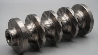 Precision-machined mud motor rotor showing helical steel lobes, harsh industrial shadows, metallic reflection