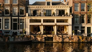 A historic canal-side boutique hotel in Amsterdam, warm golden hour light reflecting on the water, elegant European heritage, 35mm