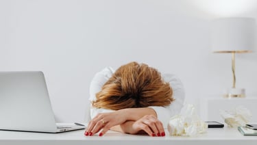 a woman with her head in her hands, sitting at a desk with a laptop