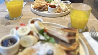 Assiettes de brunch avec pancakes, fruits, gaufres, confitures et verres de jus d’orange.