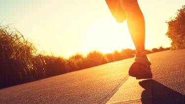 a person is running on a road with the sun setting