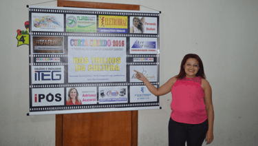 Carmelita Gomes, produtora do curta canedo aponta para o banner do curta canedo 2016