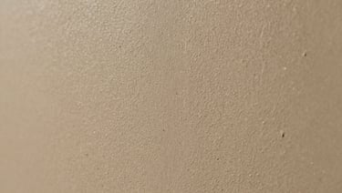 Macro detail of hand-troweled microcement texture, warm sand tone, soft directional light highlighting the subtle mineral ridges.