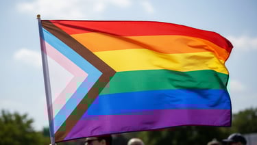 A close-up of a vibrant rainbow pride flag held up against a daylight sky.