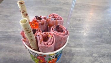 Handmade strawberry rolled ice cream in a cup with sprinkles and wafer rolls.