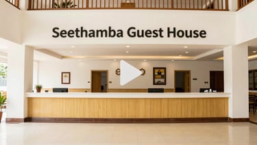 Wide panoramic view of Seethamba Guest House lobby, styled as a video player preview with a subtle play icon overlay in the center
